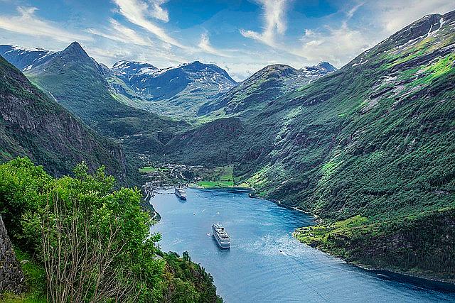 A cruise ship navigating a calm, deep fjord surrounded by massive cliffs in Norway.